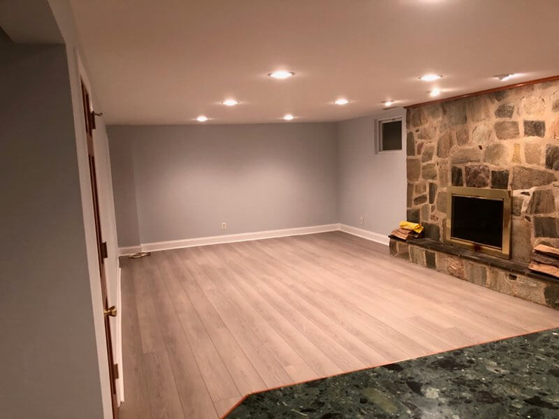 Spacious basement room with stone fireplace and recessed lighting.